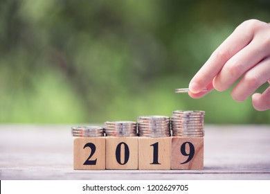 Asian Kid's Hand Putting Coins To Stack Of Coins On Wooden Block With Text 2019. Concept Of Money Saving, Financial, New Year Resolution.