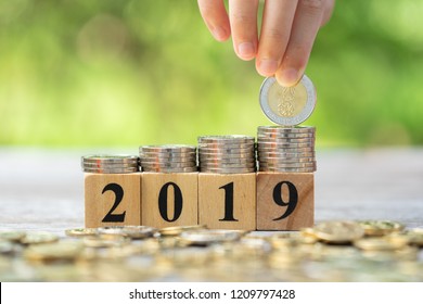 Asian Kid's Hand Putting Coins To Stack Of Coins On Wooden Block With Text 2019. Concept Of Money Saving, Financial, New Year Resolution.