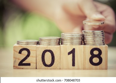 Asian Kid's Hand Putting Coins To Stack Of Coins On Wooden Block With Text 2018. Concept Of Money Saving, Financial, New Year Resolution.