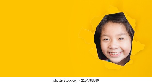 Asian Korean girl with funny face smile spy kid yellow paper break through banner.watching stubborn, kid child smile happy emotion.eye care in kid.crafty.happy child.School kid.stubborn tween girl.