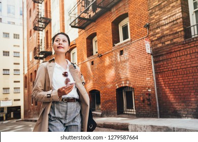 Asian Lady Back To Home After Work In Afternoon. Confident Chinese Woman Holding Mobile Phone Looking Around Living In Traditional Red Brick Apartment In San Francisco. City Urban People Lifestyle