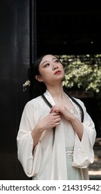 An Asian lady in Chinese vintage dress and with beautiful vintage makeup standing in the doorway of an ancient house in a sunny spring day. 