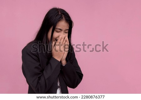 An asian lady employee breaks into laughter after hearing a funny joke. Isolated on a light pink background.