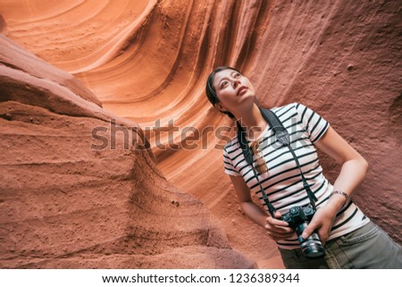 asian lady enjoying the amazing view standing in the cave surrounding with sand mountain. young girl traveler with camera looking up the sky. hiking travel in usa lifestyle concept.