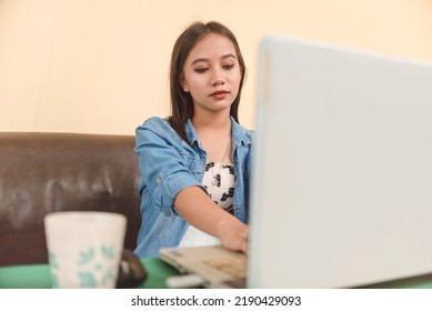 An Asian Lady In Her Early 20s Working On The Laptop. Working On A Hybrid Setup At The Living Room.