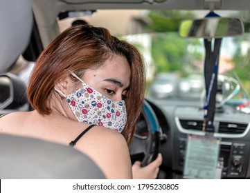 An Asian Lady Looks At The Backseat While Driving Her Car. Wearing A Cloth Face Mask. Natural Light Shot.