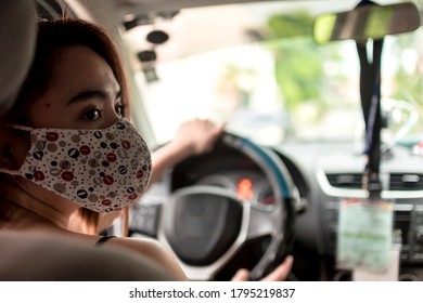 An Asian Lady Looks To Her Right While Driving Her Car. Wearing A Cloth Face Mask. Natural Light Shot.