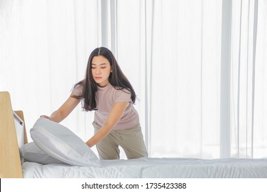Asian lady making bed in her morning routine after wake up for tidying up the bedroom in soft light with copy space - Shutterstock ID 1735423388
