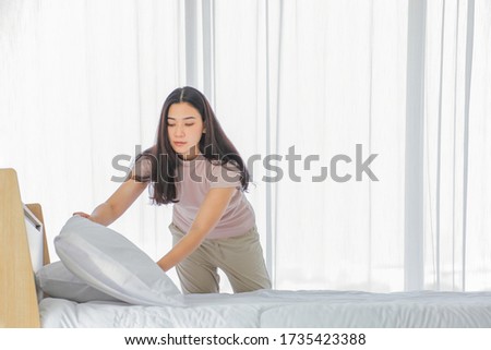 Asian lady making bed in her morning routine after wake up for tidying up the bedroom in soft light with copy space