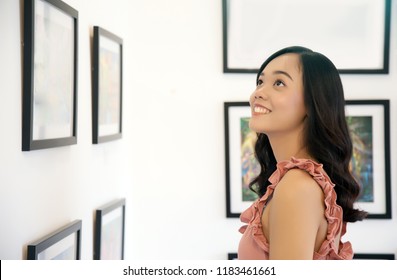 Asian Lady Watch At Photo Frame On Wall In Studio Art Gallery. 