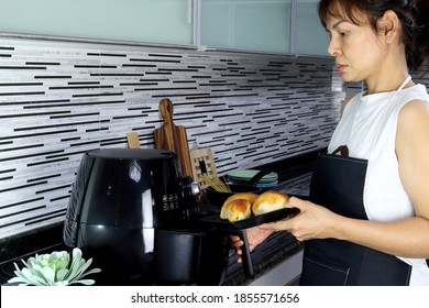 An Asian Lady Woman Is Baking Some Butter Cheese Breads For Her Breakfast By Using A Black Air Fryer Machine In The Nice Interior Design Kitchen
