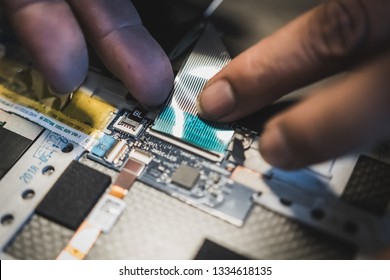 Asian laptop repair technician plugging in a ribbon cable which connect circuit boards and components in a laptop together - Shutterstock ID 1334618135