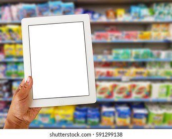 Asian Left Hand Holding Blank Tablet Screen On Blurred Various Brand Of Tissue Paper And Diaper In Packaging For Sale On Supermarket Stand Or Shelf 
