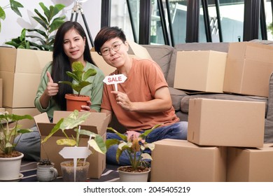 An Asian Lesbian Couple Runs An Online Plant Selling Business. Help Pack It Into A Cardboard Box And Send It To The Customer. The Concept Of Married Young Same-sex Couples Living Together.