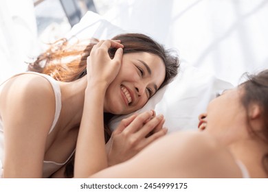 Asian lesbian couple smiling and lying close together in bed, enjoying a loving, intimate moment - Powered by Shutterstock