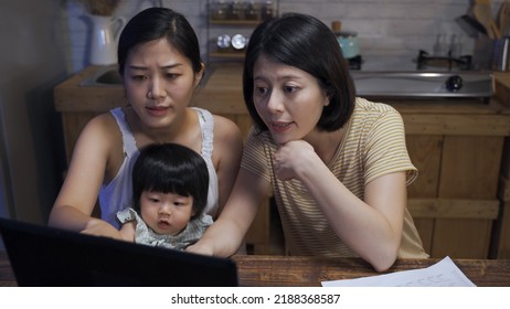 Asian Lgbtq Family With Their Adopted Daughter Are Having Discussion While Using Laptop To Make Tax Payment Online In The Dining Room At Night.