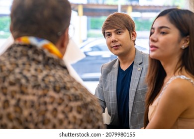 Asian LGBTQ Guy Bridal Shop Owner Using Laptop Help Male And Female Couple Customer Choosing Wedding Gown And Suit At Wedding Studio. Small Business Entrepreneur Wedding Planner And Marriage Concept