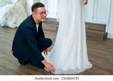 Asian LGBTQ Guy Bridal Shop Owner Helping Female Bride Customer Choosing And Trying On Wedding Gown At Wedding Studio. Small Business Entrepreneur Wedding Planner And Marriage Ceremony Concept