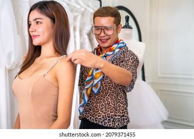 Asian LGBTQ Guy Designer Bridal Shop Owner Measuring Female Bride Customer For Making Wedding Gown In Fitting Room At Wedding Studio. Small Business Tailor Entrepreneur And Wedding Planner Concept