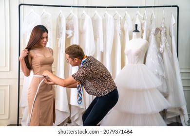 Asian LGBTQ Guy Designer Bridal Shop Owner Measuring Female Bride Customer For Making Wedding Gown In Fitting Room At Wedding Studio. Small Business Tailor Entrepreneur And Wedding Planner Concept