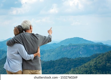 Asian Lifestyle Senior Couple Hug And Pointing The Mountain Nature.  Old People Happy In Love Romantic And Relax Time.  Tourism Family Elderly Retirement Travel In Summer Leisure And Destination.