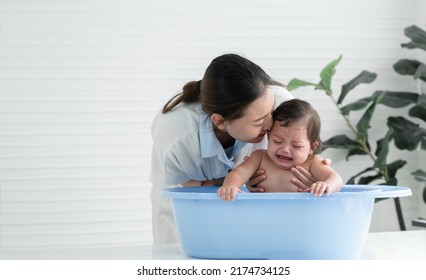 Asian Little Baby Crying With Screaming Face Sitting In Bathtub With Young Mother Is Kissing Comforting Her Child While Mom Bathing Her Cute Daughter At Home. Baby Bathing Concept. White Background