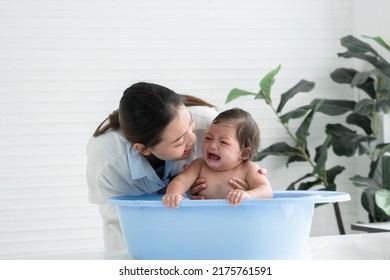 Asian Little Baby Crying With Screaming Face Sitting In Bathtub With Young Mother Is Comforting Her Child While Mom Bathing Her Cute Daughter At Home. Baby Bathing Concept. White Background