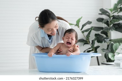 Asian little baby crying with screaming face sitting in bathtub with young mother is comforting her child while mom bathing her cute daughter at home. Baby bathing concept. White background - Shutterstock ID 2176327399