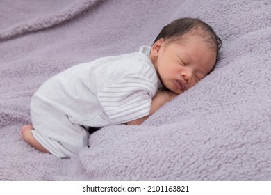 Asian Little Baby Curled Up Sleeping On A Blanket. Adorable Newborn Baby Wearing White Casual Clothes Lying On Grey Blanket With Happy And Safe. Newborn Baby Aged 0-1 Months Lying In Bed.
