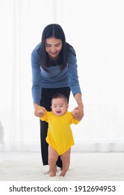 Asian Little Baby Girl Taking First Steps Learning To Walk With Mom Help Support The Cute Unstable Walking Toddler At Home In Bedroom. Happy Family First Steps Parenthood Concept