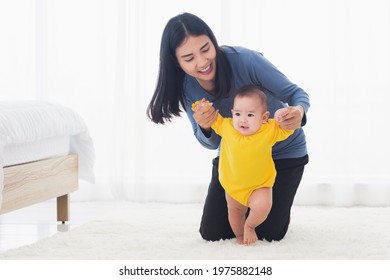 Asian Little Baby Girl Taking First Steps Learning To Walk With Mom Help Support The Cute Unstable Walking Toddler At Home In Bedroom. Happy Family First Steps Parenthood Concept