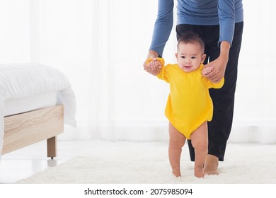 Asian Little Baby Taking First Steps Learning To Walk With Mother Help Support The Cute Unstable Walking Toddler. Happy Family First Steps Parenthood Concept