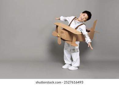 Asian little boy aviator playing with cardboard airplane isolated on grey background, Kid toy diy concept - Powered by Shutterstock