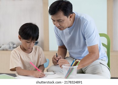 Asian Little Boy Drawing On Pages With Colour Pencils On Table At Classroom. Kid Learning By Drawing. Education Concept