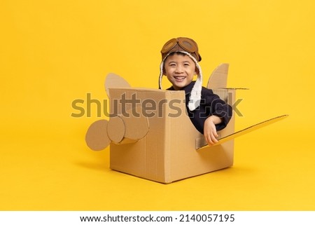 Asian little boy playing with cardboard airplane isolated on yellow background