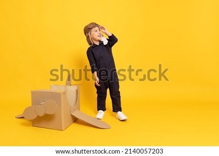 Asian little boy playing with cardboard airplane isolated on yellow background