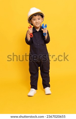 Asian little boy playing and showing repair tool isolated on yellow background, Technician kid concept
