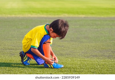 Asian little Boy in Soccer Uniform tying shoelace on soccer Field before training - Powered by Shutterstock