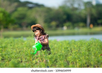 Asian Little Child Girl Or Kid Pouring Water On The Trees. Kid Helps To Care For The Plants With A Watering Can In The Garden.