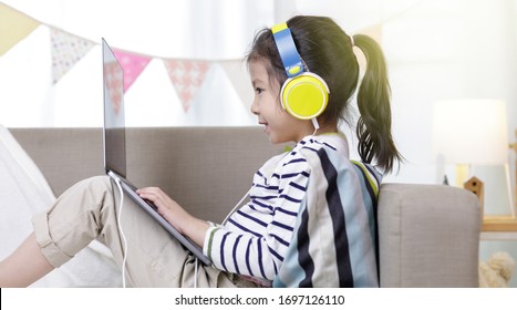 Asian little child girl learning at home wear headphone talk video calling with laptop meeting online app, Quarantine isolation during the Coronavirus (COVID-19) health care, online education concept