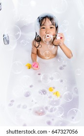 Asian little Chinese girl blowing bubbles in bathtub at home