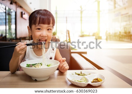 Asian little Chinese girl eating beef noodles soup in outdoor cafe