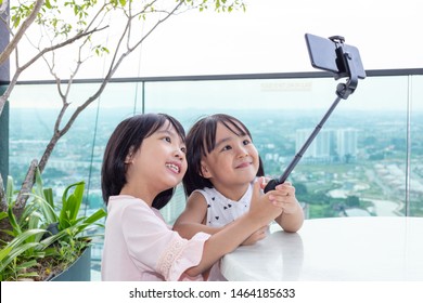 Asian Little Chinese Sisters taking selfie with smartphone on selfie stick in the outdoor cafe