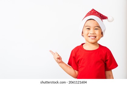 Asian Little Cute Child Boy Smile And Excited, Kids Dressed In Red Santa Claus Hat Point Finger To Side Away The Concept Of Holiday Christmas Xmas Day Or Happy New Year, Isolated On White Background