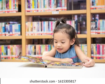 Asian Little Cute Girl 3-4 Years Old Sitting On Chair And Looking A Kid's Book At The Library. Learning And Education Of Kid.