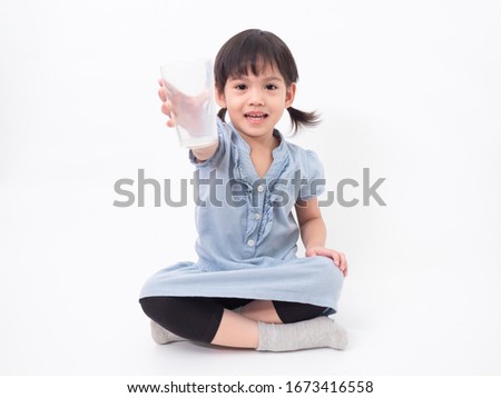 Asian little cute girl 4 years old holding empty glass after drink all the milk  on white background. Milks is essential and nutrition for the child's body.
