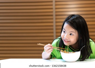 Asian Little Cute Girl Eating Delicious Instant Noodles With Chopstick By Herself On Wooden Curtain Background.Food,Family,Childhood Concept.Instant Noodles Is A Convenient,delicious And Cheap Food.