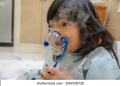 Asian Little Cute Girl With Influenza Hospital Admission. 
Kid Patient Holding  The Mask Of Inhaler, Getting Bronchodilator.
