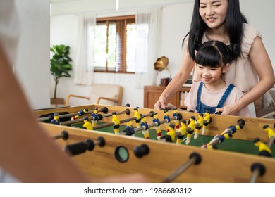 Asian Little Cute Kid Daughter Having Fun Spend Free Leisure Time With Parents In House. Young Preschool Girl Enjoy Playing Table Soccer Or Football Game With Father And Mother In Living Room At Home.