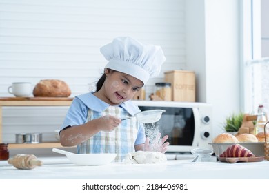 Asian Little Cute Kid Girl Wear Chef Hat And Apron With Flour Mess Up On Face Have Fun Sifting Flour On Dough Bread In Kitchen At Home Or Baking Class At School. Child Education Concept